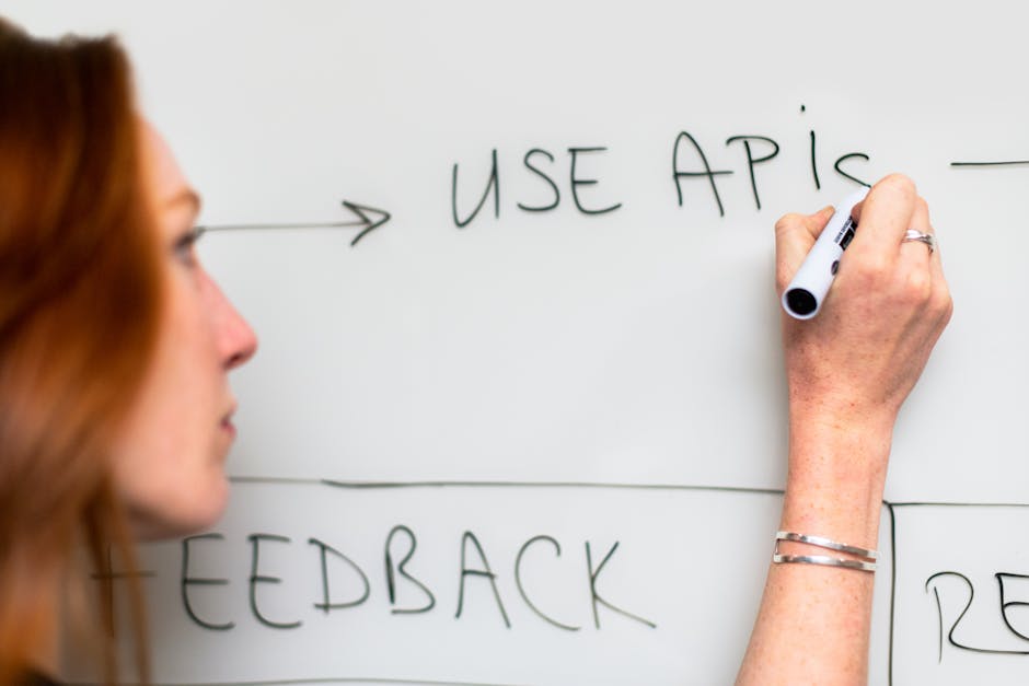 A woman writes 'Use APIs' on a whiteboard, focusing on software planning and strategy