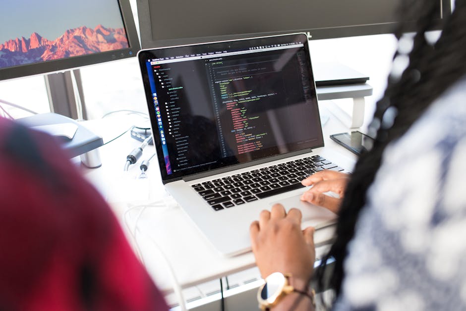 A woman coding on a laptop in a modern office environment with multiple monitors